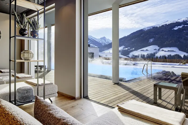 Vanuit de relaxruimte heb je een mooi uitzicht over de infinity pool, de badesee en de met sneeuw bedekte bergen van het Alpbachtal © Der Böglerhof